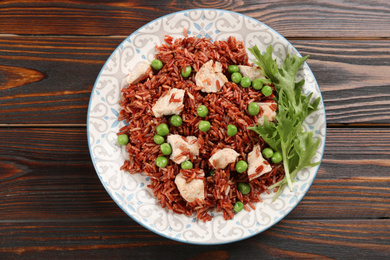 Photo of Tasty brown rice with meat and vegetables on wooden table, top view