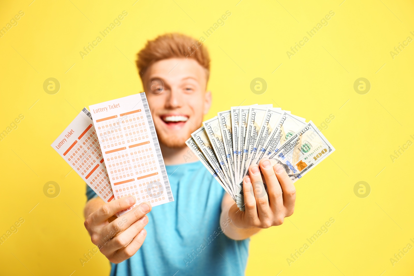 Photo of Happy young man holding lottery tickets and money on yellow background