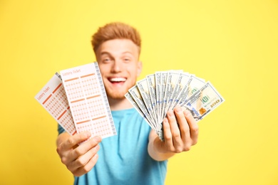 Photo of Happy young man holding lottery tickets and money on yellow background