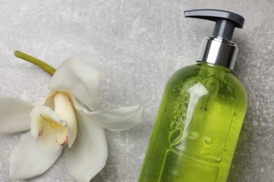 Photo of Dispenser of liquid soap and orchid flower on grey table, flat lay