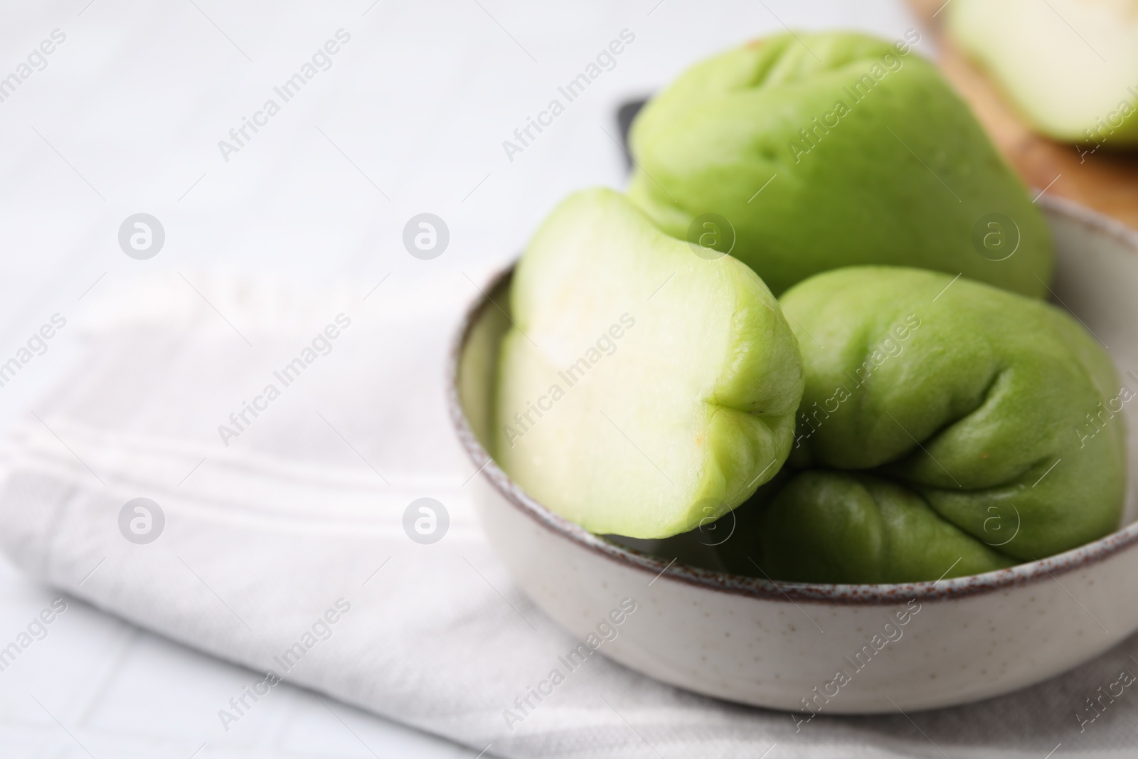 Photo of Cut and whole chayote in bowl on table, closeup. Space for text