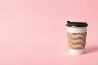 Photo of Takeaway paper coffee cup with cardboard sleeve on pink background. Space for text