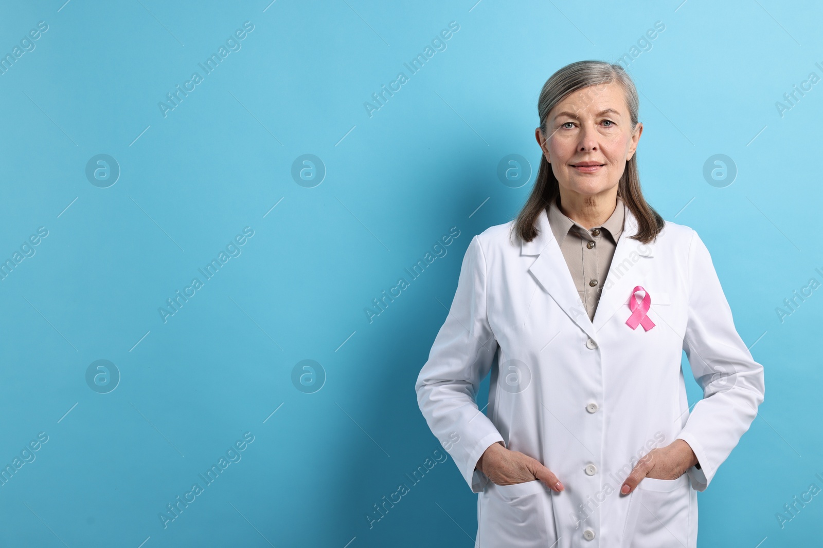 Photo of Mammologist with pink ribbon on light blue background, space for text. Breast cancer awareness