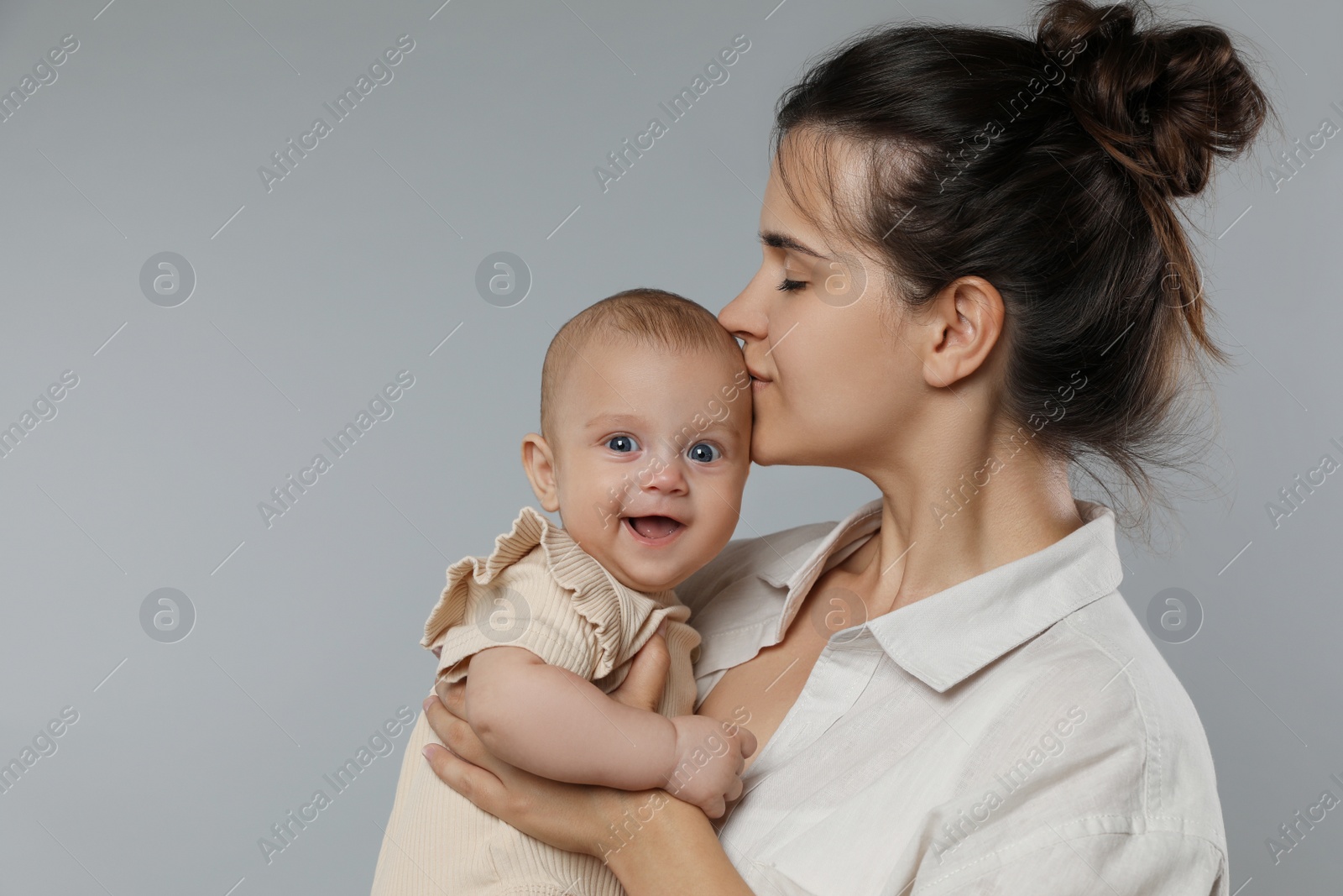 Photo of Beautiful mother kissing her cute baby on grey background. Space for text