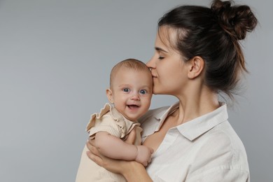 Photo of Beautiful mother kissing her cute baby on grey background. Space for text