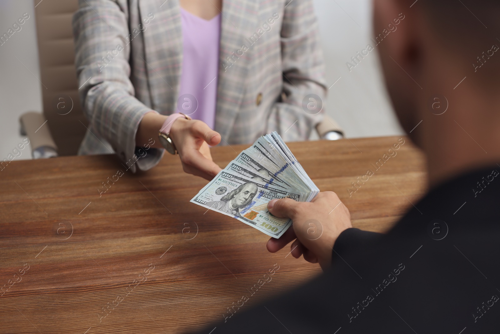 Photo of Man giving bribe money to woman at table indoors, closeup