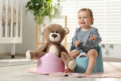 Photo of Little child and teddy bear sitting on plastic baby potties indoors