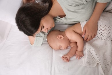 Young mother resting near her sleeping baby on bed, top view