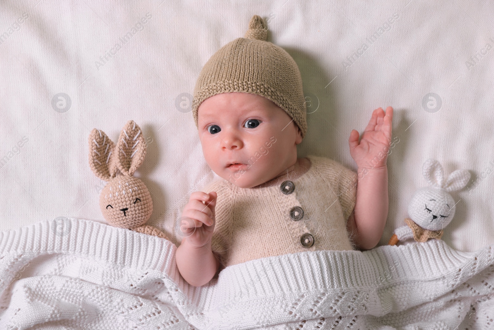 Photo of Cute newborn baby with toys on white knitted plaid, top view
