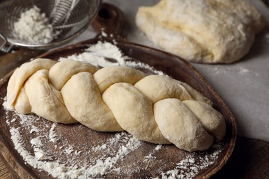 Photo of Raw braided bread and flour on wooden table, closeup. Traditional Shabbat challah
