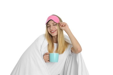 Happy woman in sleeping mask wrapped with blanket holding cup on white background