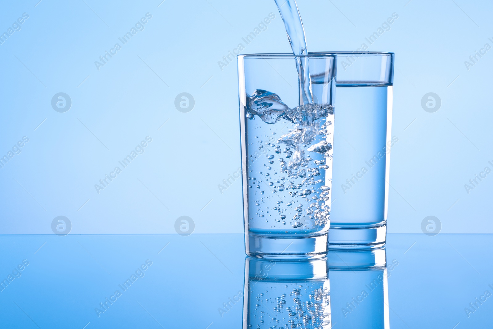 Photo of Pouring water into glass on light blue background. Space for text