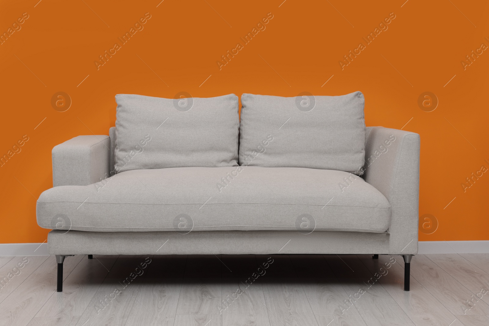 Photo of Comfortable sofa near bright orange wall indoors