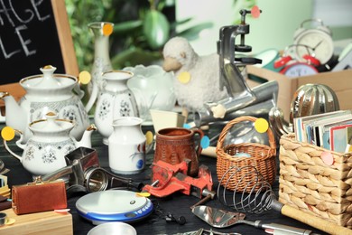 Photo of Many different stuff on black wooden table indoors. Garage sale