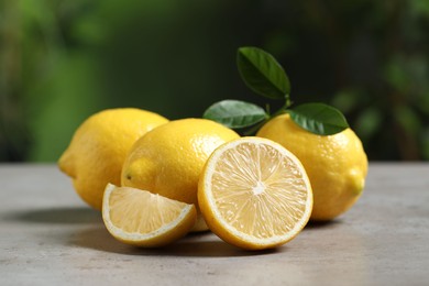 Photo of Fresh lemons and green leaves on grey table outdoors, closeup