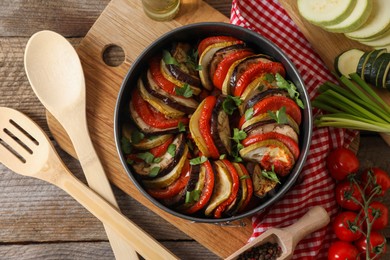 Delicious ratatouille, ingredients, spoon and spatula on wooden table, flat lay