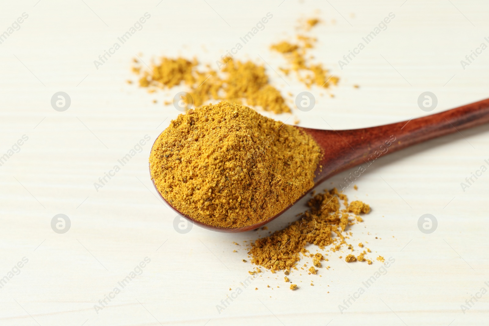 Photo of Spoon with dry curry powder on light wooden table, closeup. Space for text