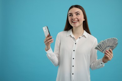 Happy woman with dollar banknotes and smartphone on light blue background, space for text