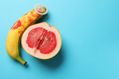 Photo of Half of grapefruit, banana with condom and red lipstick marks on light blue background, flat lay with space for text. Safe sex concept