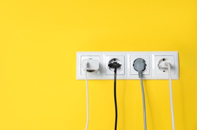 Photo of Power sockets with inserted plugs on yellow wall, space for text. Electrical supply