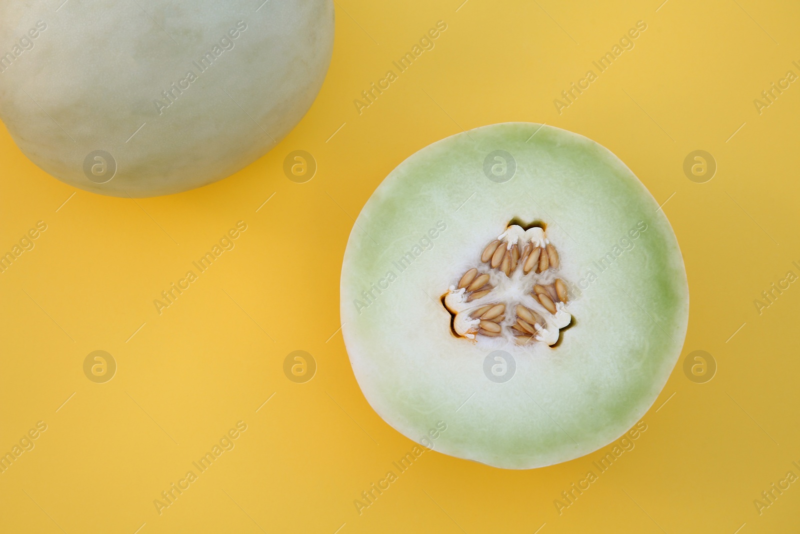 Photo of Whole and cut fresh ripe honeydew melons on yellow background, flat lay. Space for text