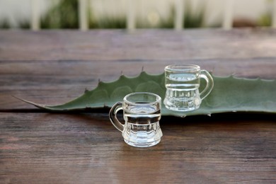 Photo of Mexican tequila shots and green leaf on wooden table. Drink made of agava