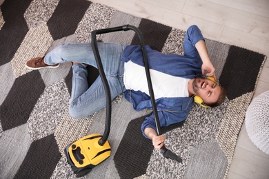 Photo of Young man having fun while vacuuming at home, above view