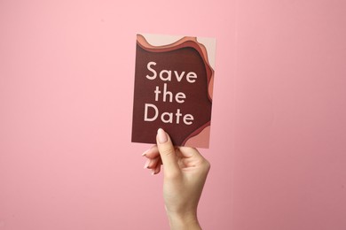 Photo of Woman holding beautiful card with Save the Date phrase on pink background, closeup