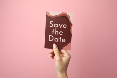 Woman holding beautiful card with Save the Date phrase on pink background, closeup