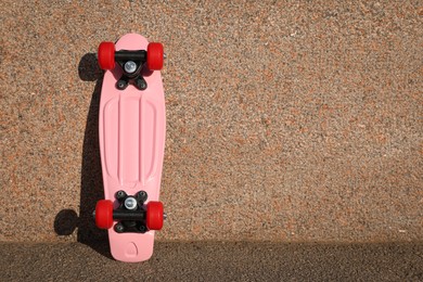 Photo of Pink skateboard with red wheels near wall outdoors. Space for text