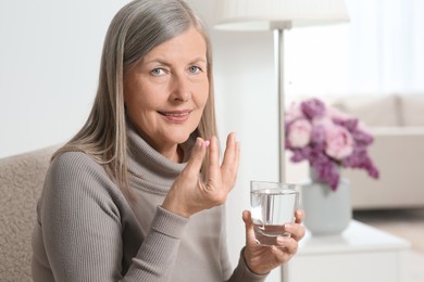 Photo of Senior woman with glass of water taking pill at home. Space for text