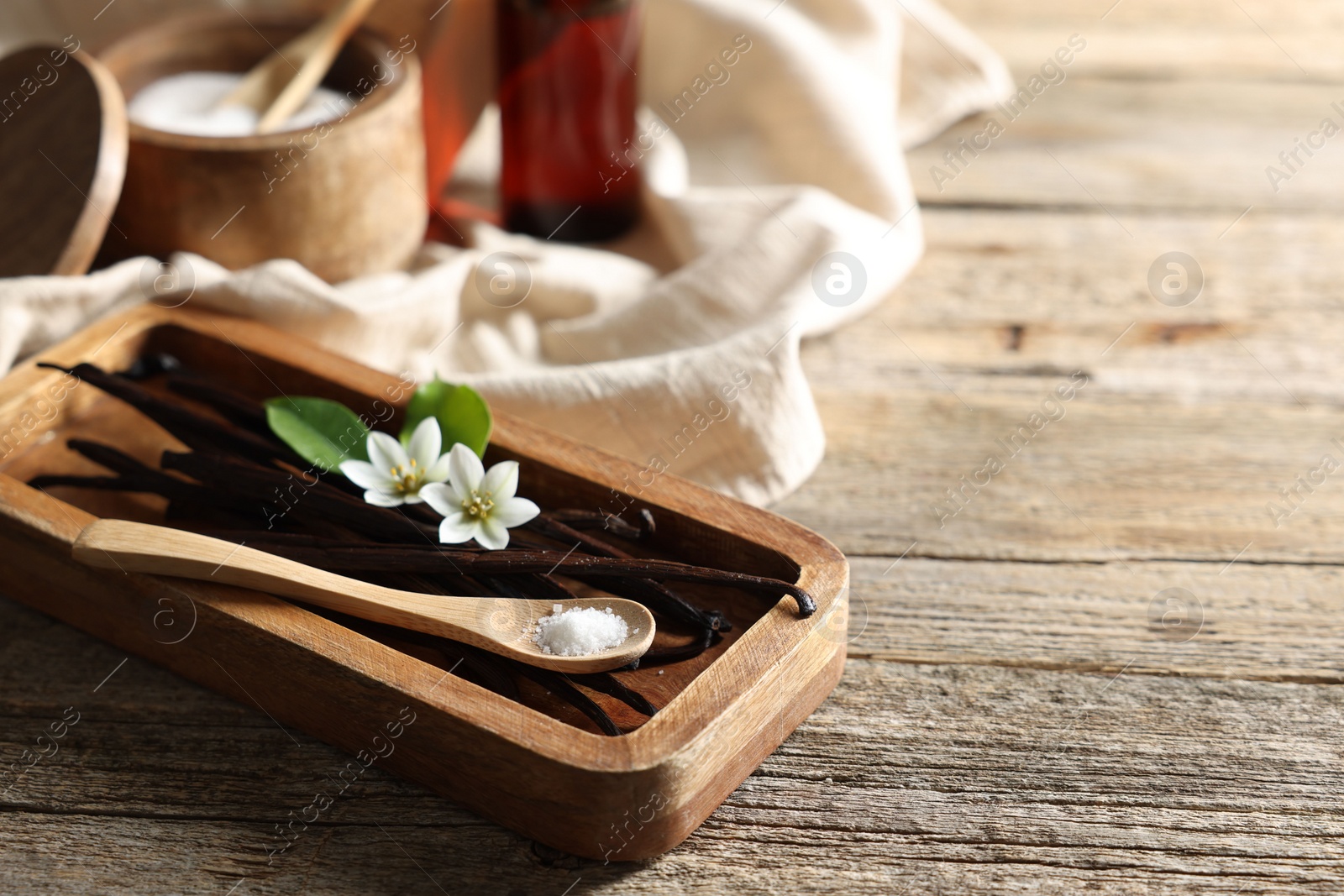 Photo of Vanilla pods, flowers, leaves and spoon with sugar on wooden table, closeup. Space for text