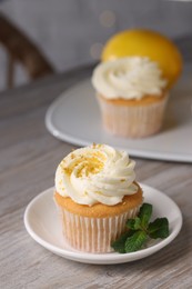 Photo of Delicious lemon cupcake with white cream and mint on table, closeup