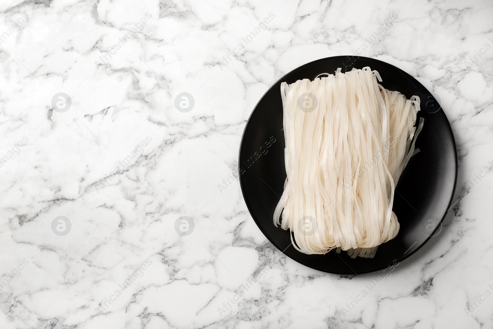 Photo of Plate with raw rice noodles on marble background, top view. Space for text
