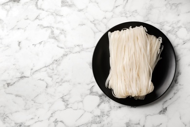 Plate with raw rice noodles on marble background, top view. Space for text