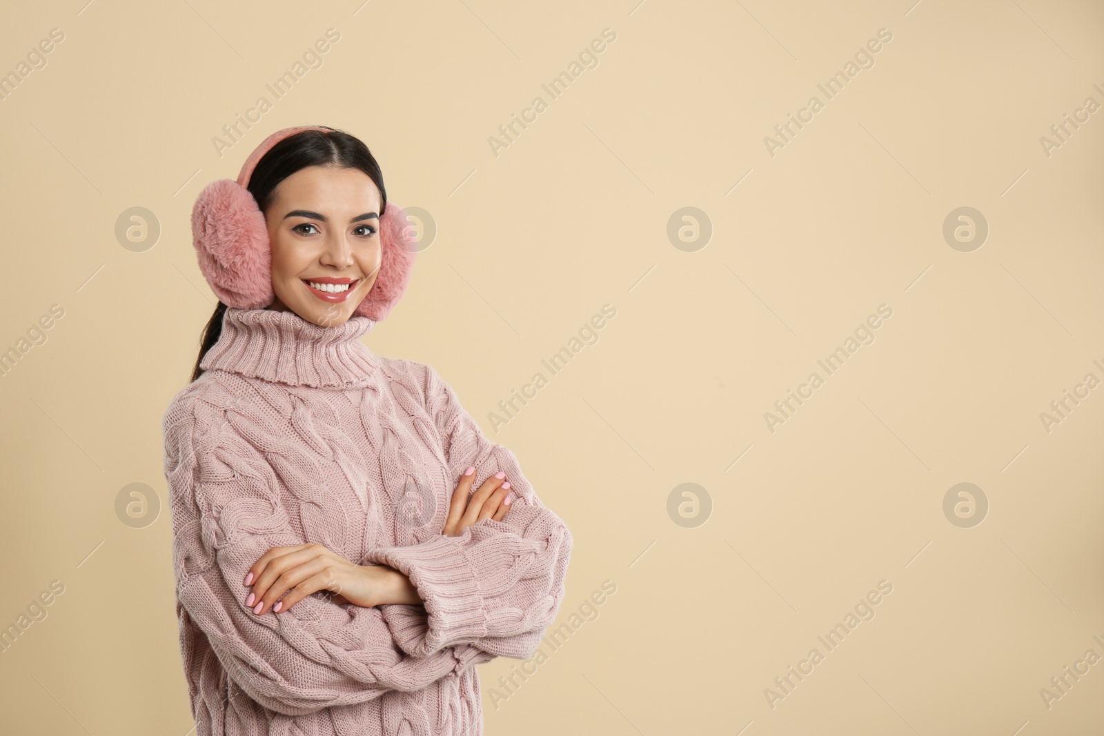 Photo of Beautiful young woman wearing earmuffs on beige background. Space for text