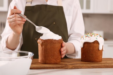 Woman decorating traditional Easter cake with glaze at white marble table in kitchen, closeup