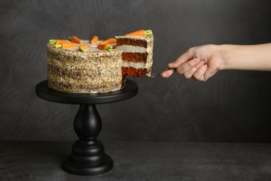 Photo of Woman taking piece of carrot cake on grey background, closeup