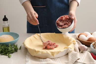 Photo of Woman putting meat into baking dish with dough to make pie at light grey table, closeup