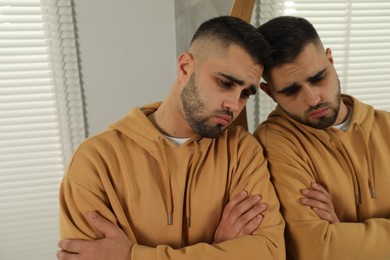 Sad young man near mirror at home