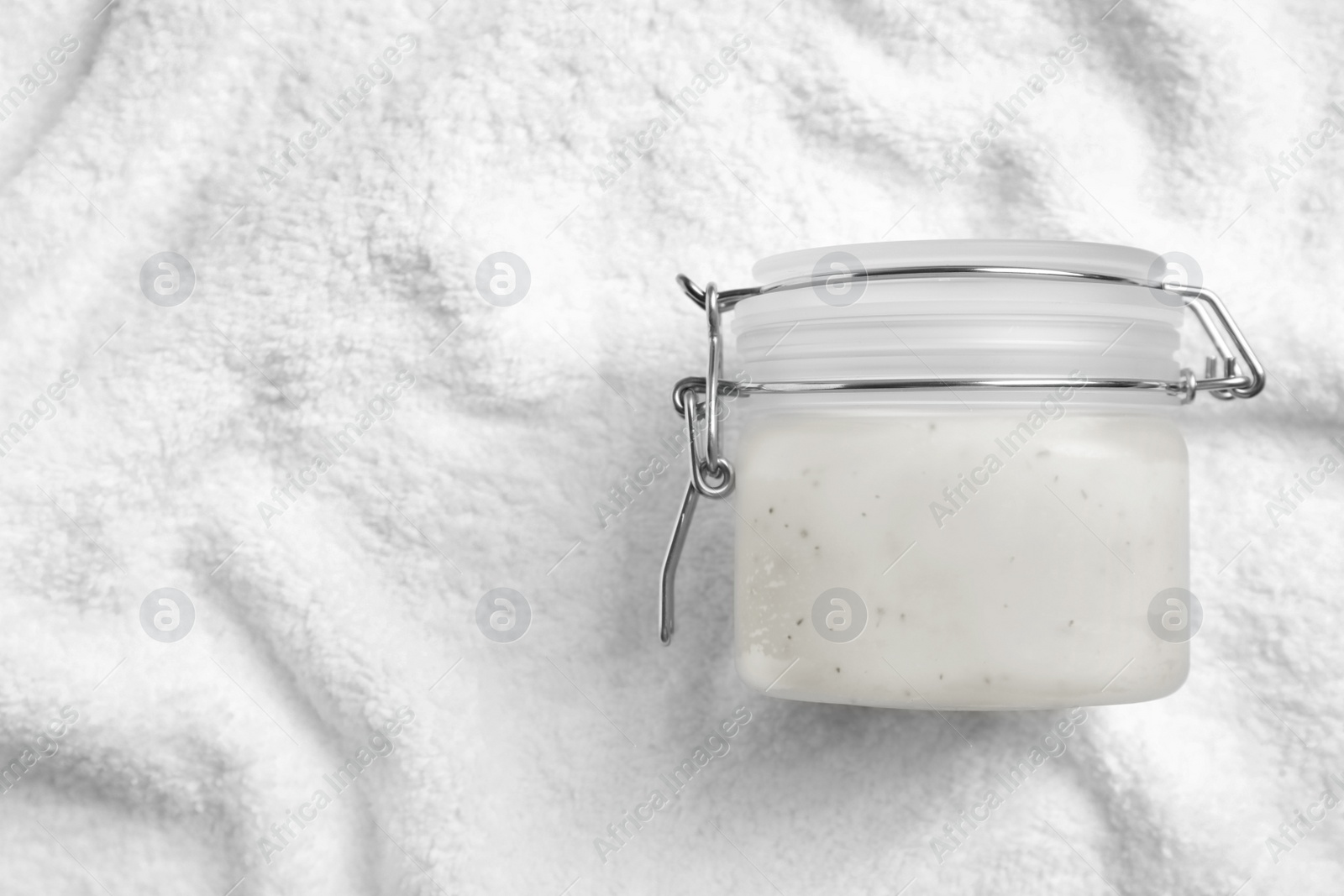 Photo of Jar of salt scrub on white towel, top view. Space for text