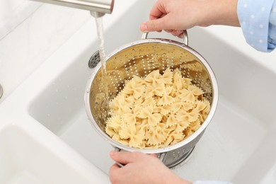 Woman rinsing pasta in colander above sink, closeup