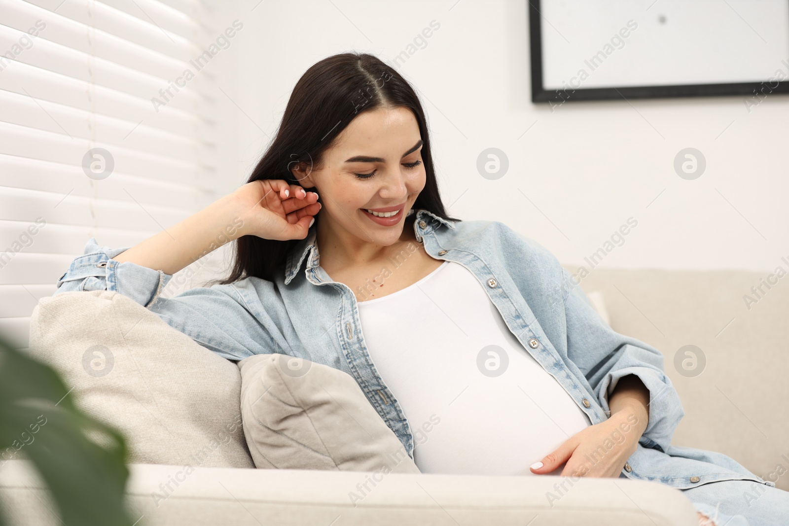 Photo of Happy pregnant woman on sofa at home