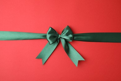 Green satin ribbon with bow on red background, top view