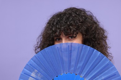 Photo of Woman hiding her face behind hand fan on purple background