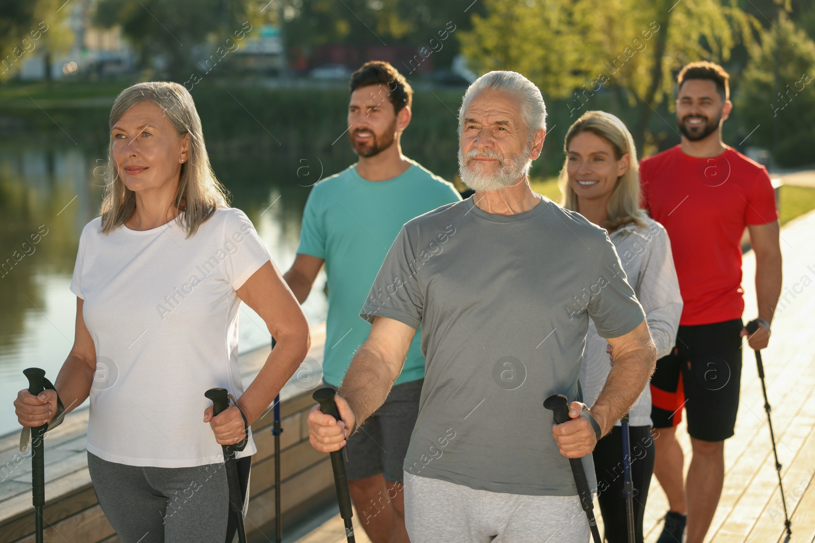 Photo of Group of people practicing Nordic walking with poles outdoors on sunny day