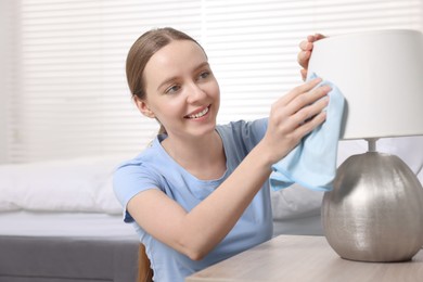 Photo of Woman with microfiber cloth cleaning lamp in bedroom