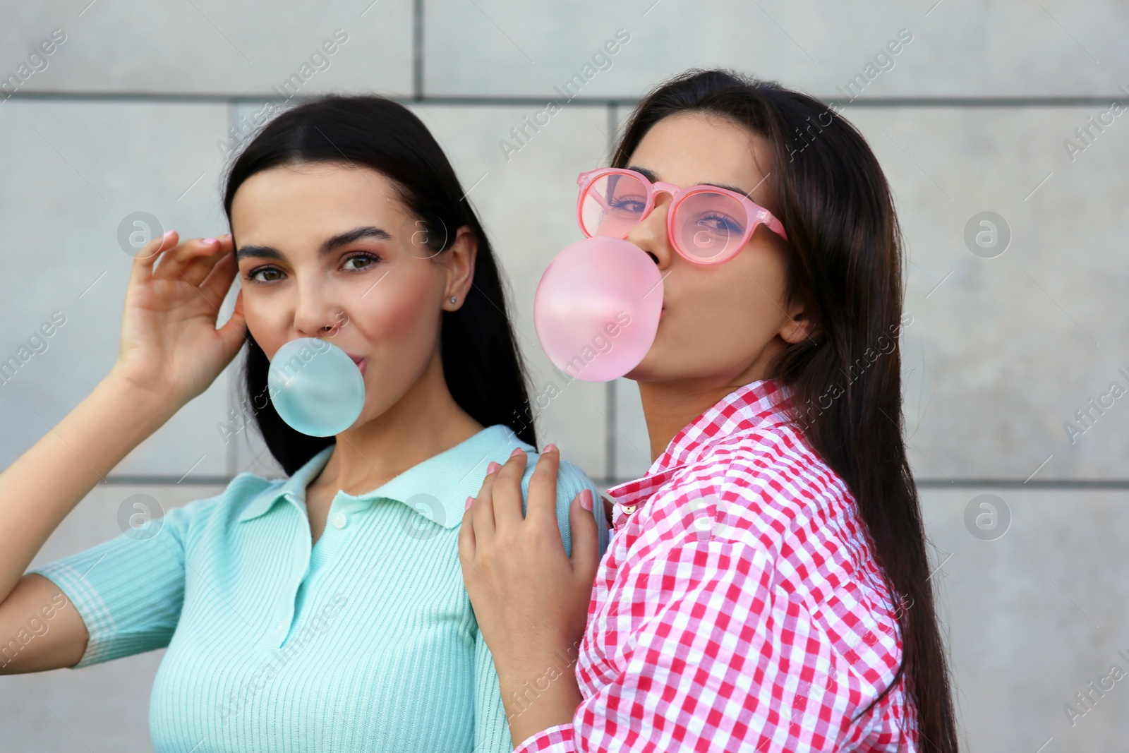 Photo of Beautiful women blowing gums near wall outdoors