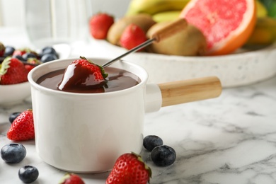 Photo of Fondue pot with chocolate and fresh berries on white marble table, closeup. Space for text