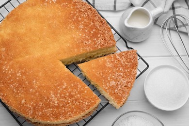 Photo of Tasty sponge cake, whisk and ingredients on white wooden table, flat lay